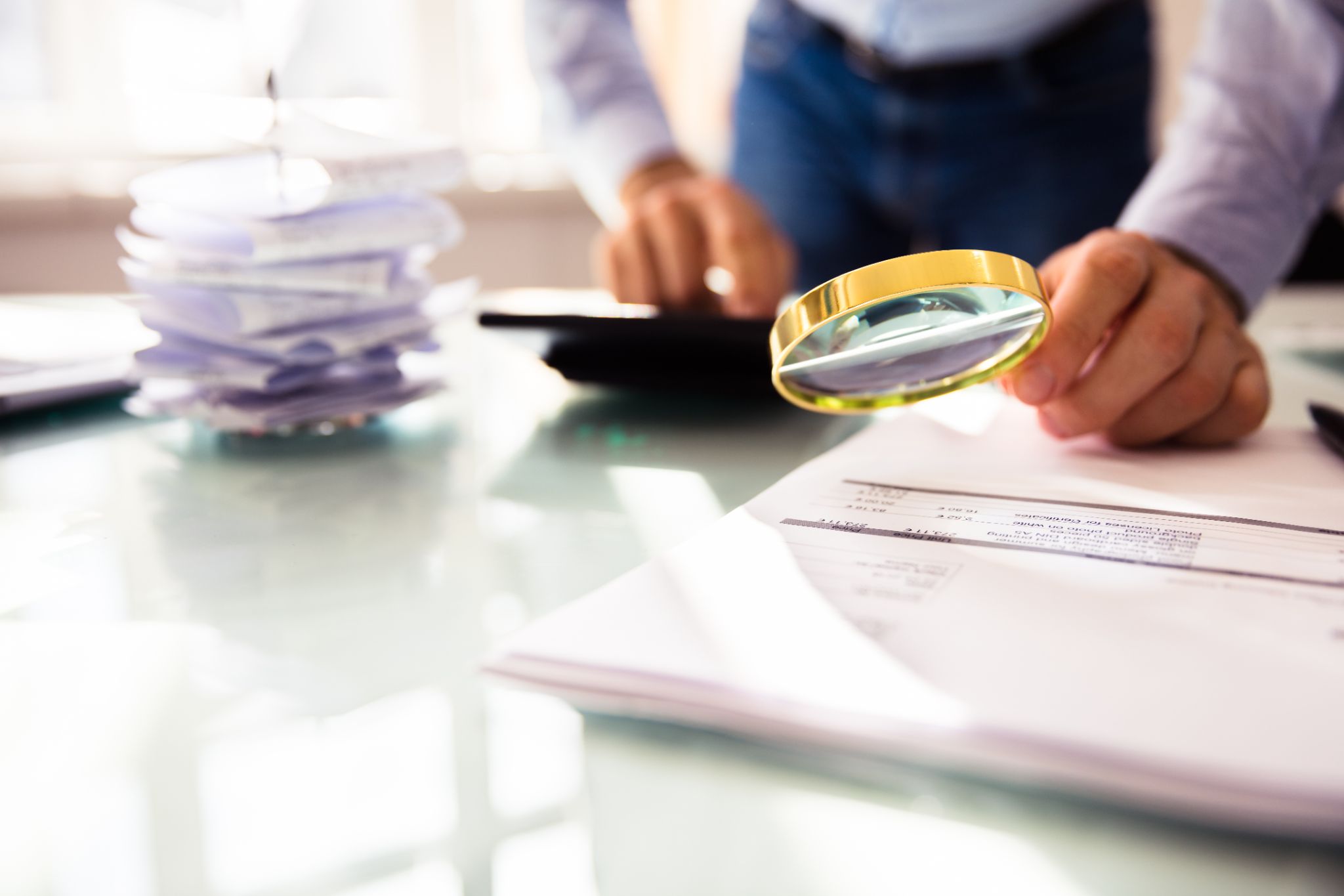 A man leaning over a printout of financial documents with a calculator and magnifying glass. Our dedicated team of Houston fraud lawyers is experienced in the nuances of criminal fraud defense.