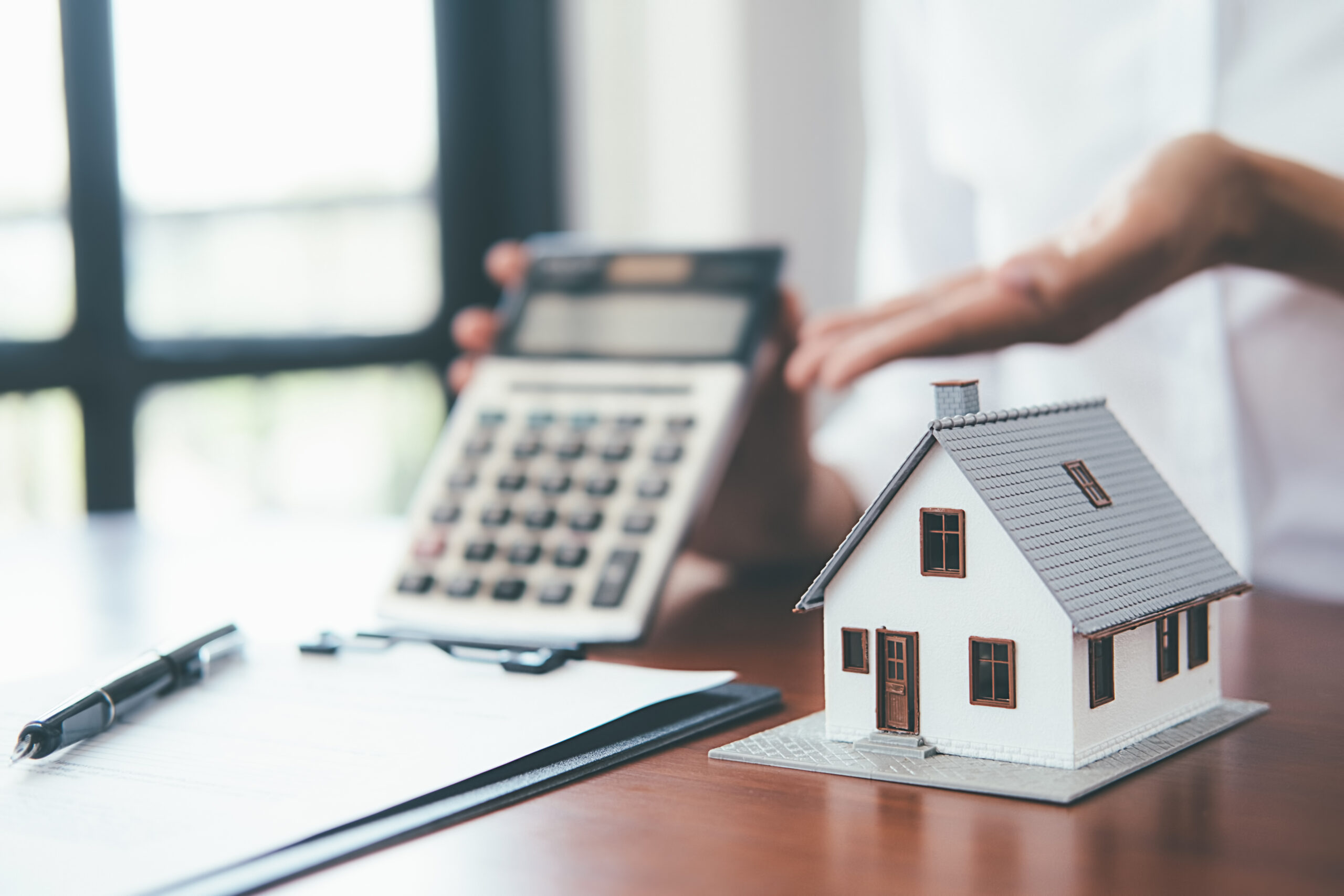 model house on desk next to contract and calculator representing mortgage. Our Houston bank fraud lawyers defend those facing mortgage fraud charges.