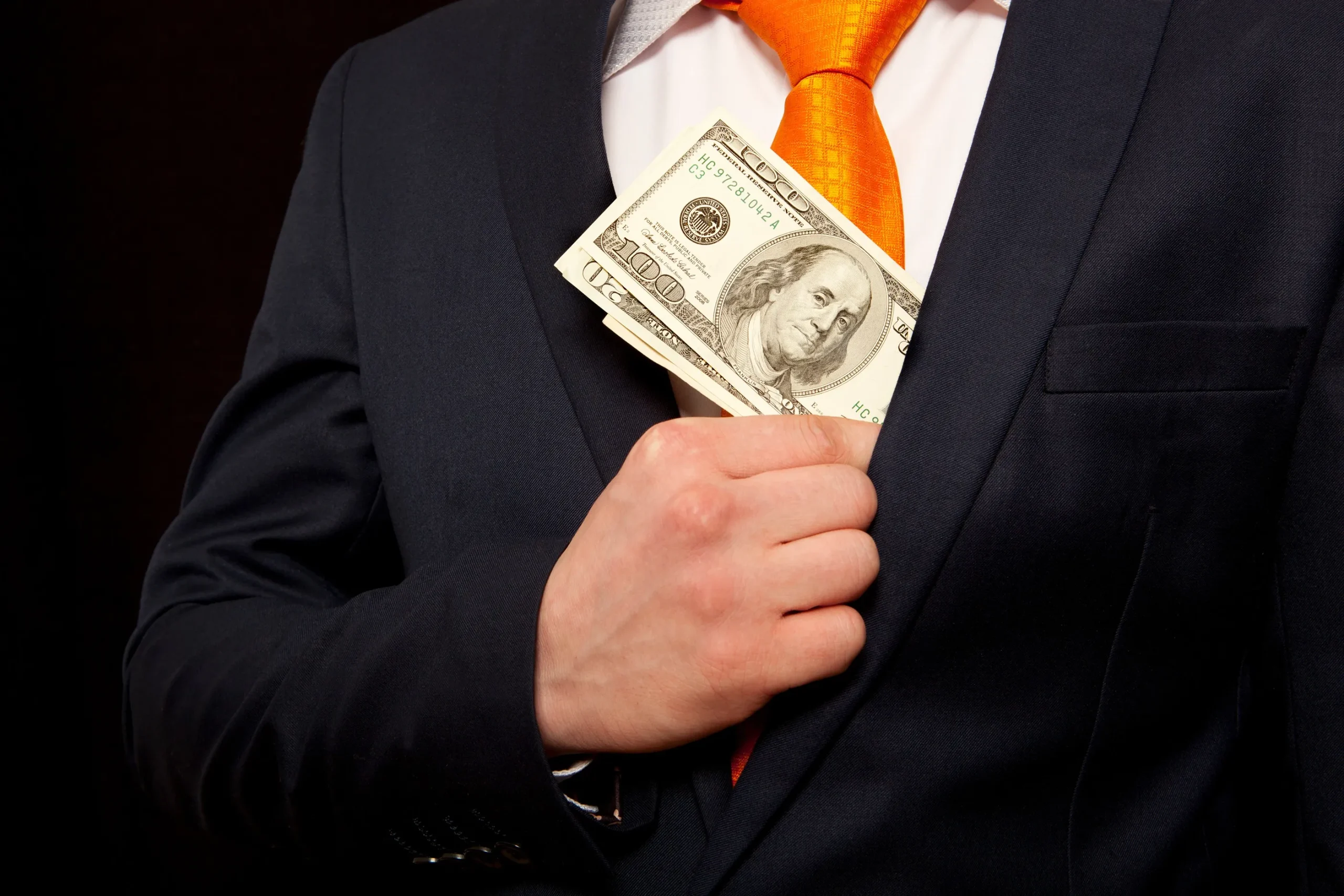 A man tucking money into his suit jacket.