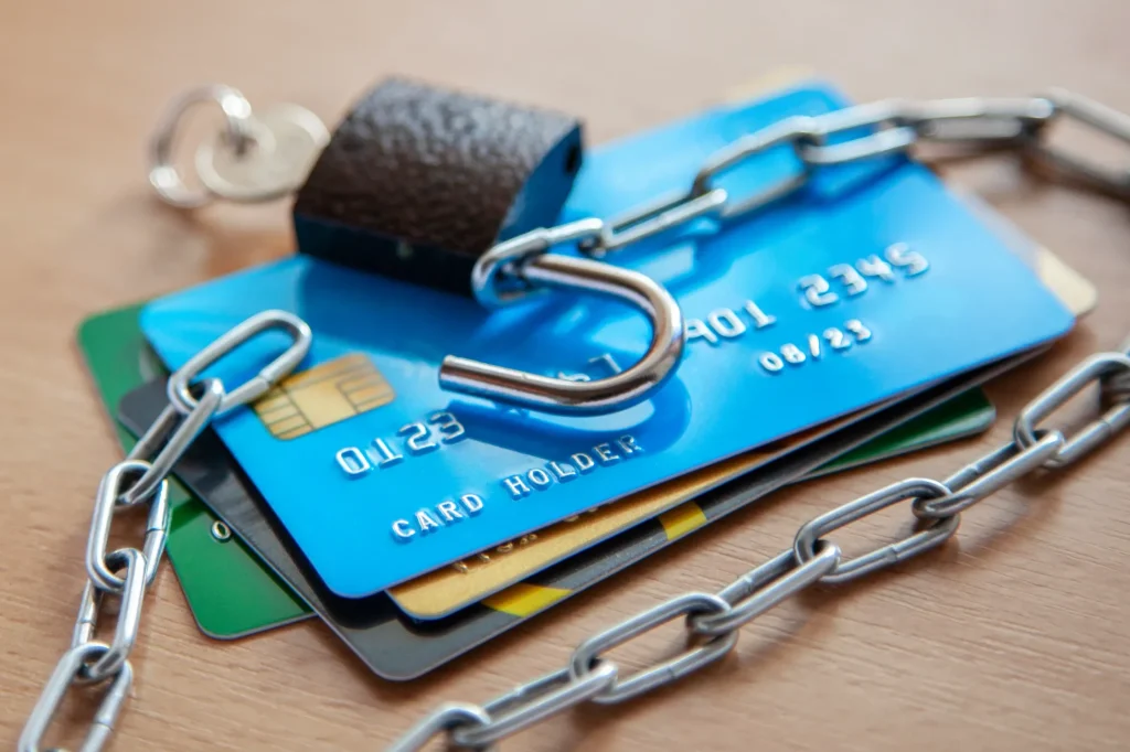 Close-up of several credit cards wrapped in a metal chain with an unlocked padlock, symbolizing identity theft or credit fraud protection.